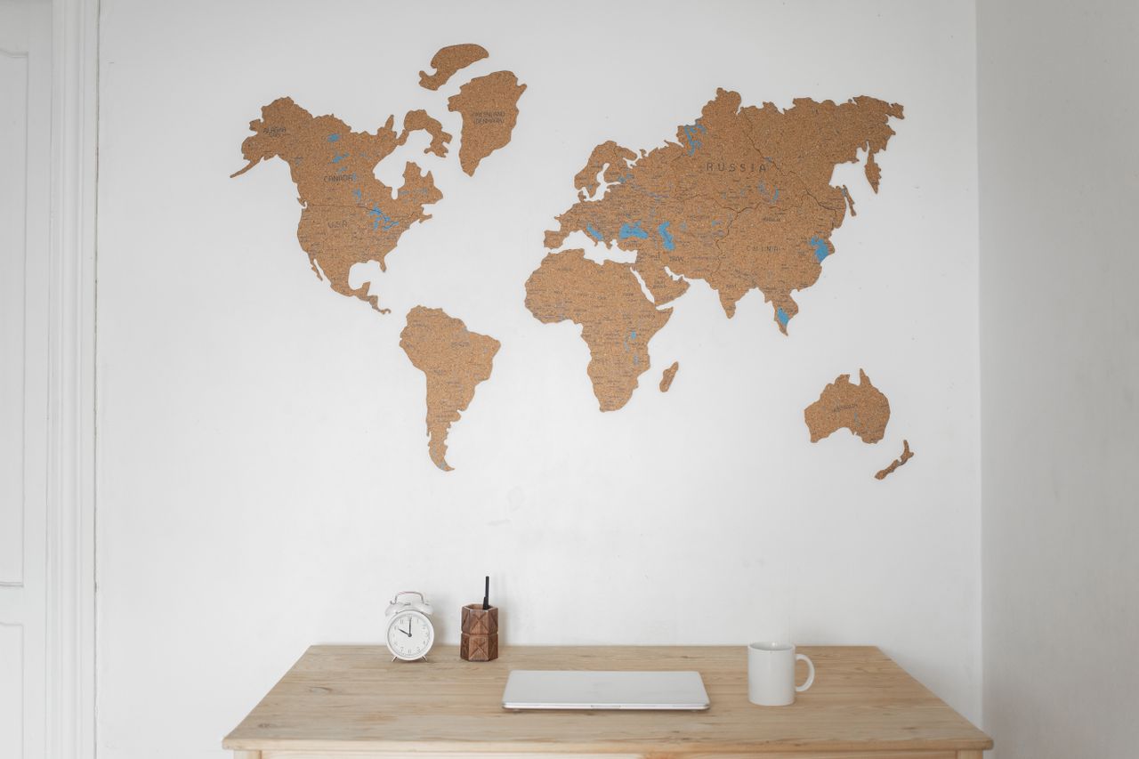 About Alarm clock near pen container with cup and laptop on table placed near silhouettes of world map on wall